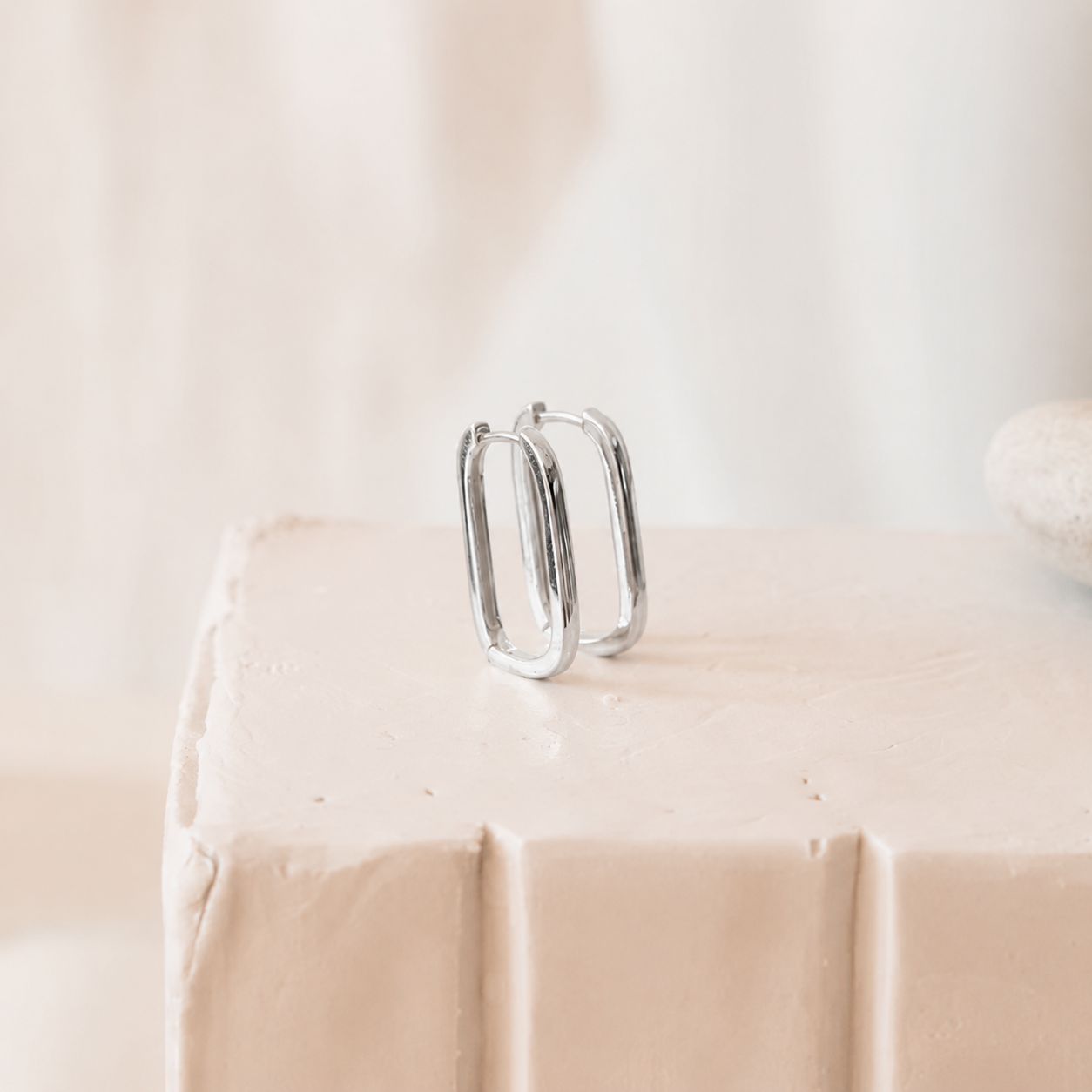 Silver hoop earrings on a beige surface with a blurred background